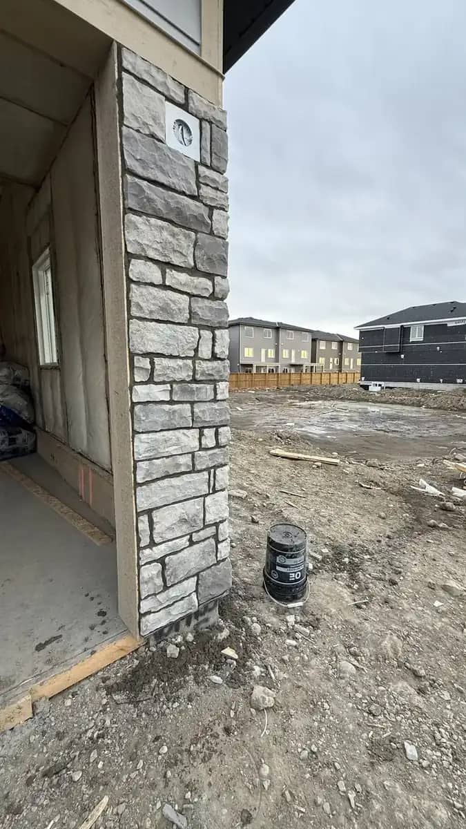 Close view of grey ledgestone wrapping a garage corner beside concrete and siding