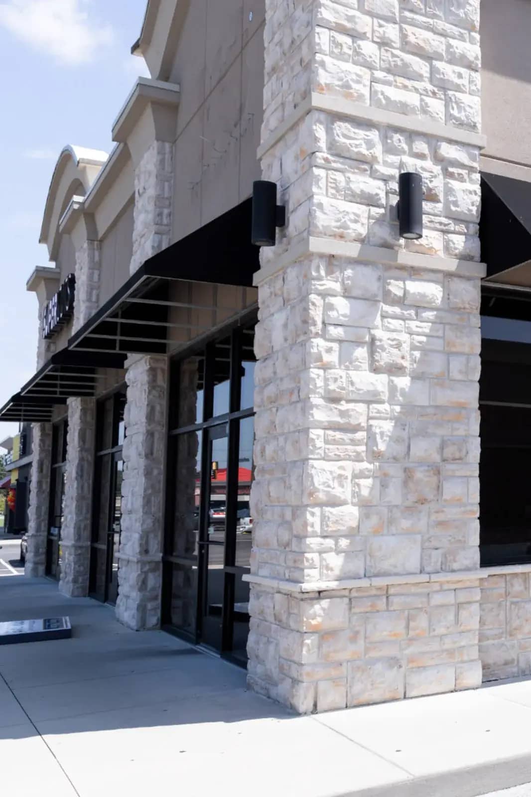 Commercial storefront with light stone masonry columns, black awnings, glass windows, and concrete sidewalk frontage