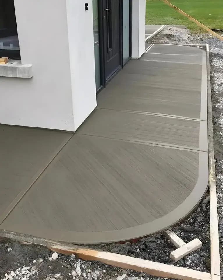 Curved broom-finished concrete walkway beside a home exterior and landscape edge