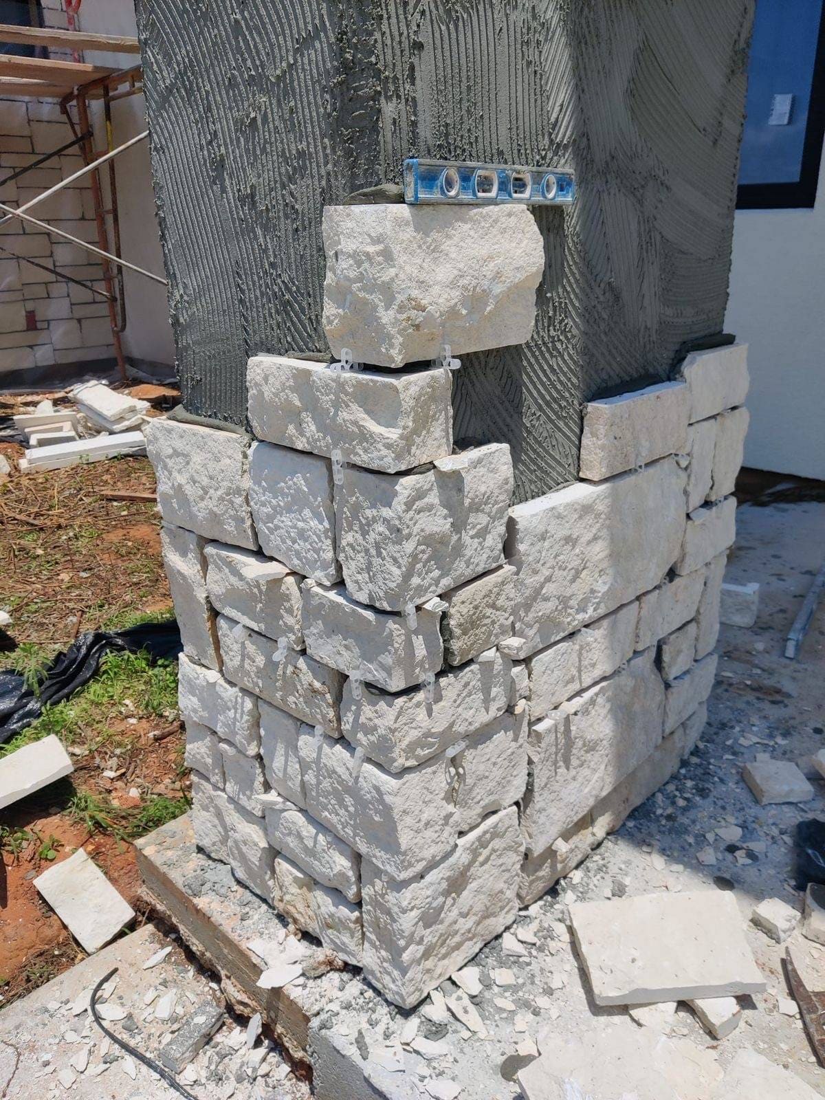 Stacked stone column under restoration with fresh mortar bed and a level set on the top course