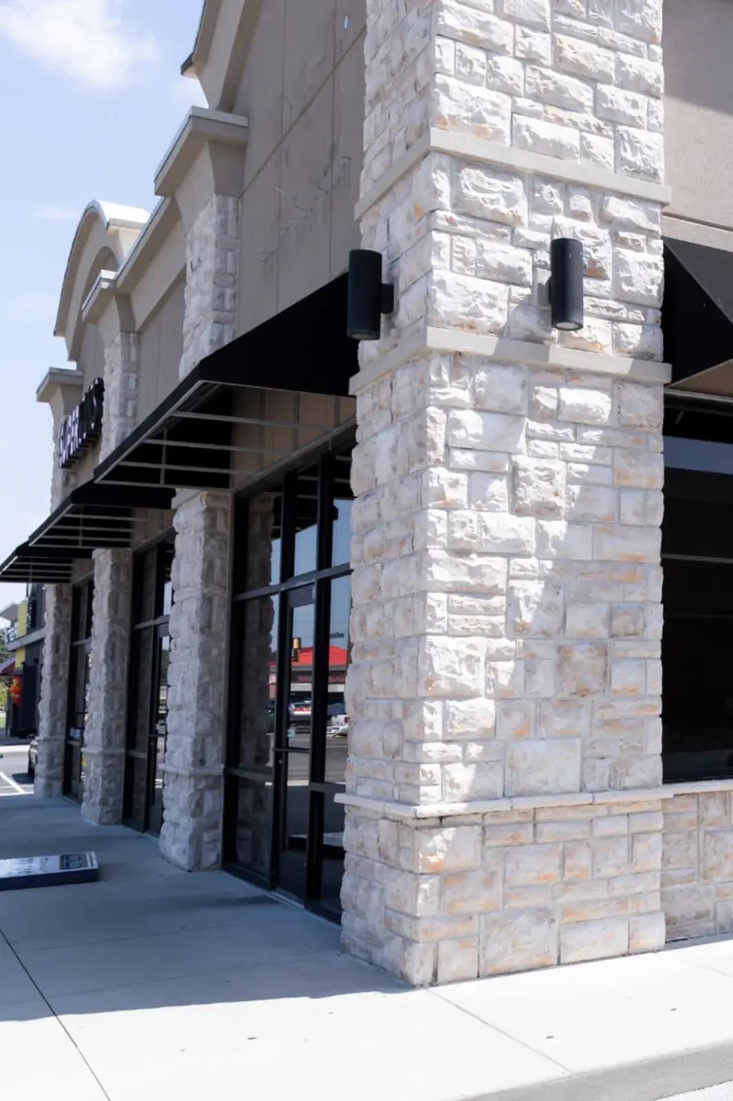 Commercial storefront with light stone masonry columns, black awnings, glass windows, and concrete sidewalk frontage