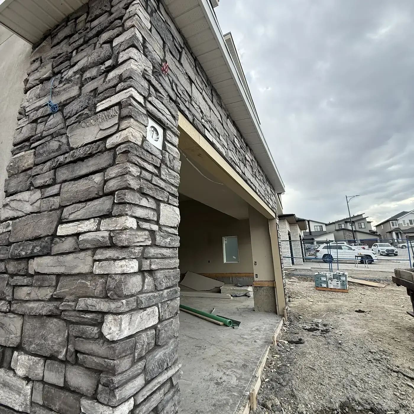 Stacked grey stone wrapping a garage return beside a residential garage opening and driveway approach