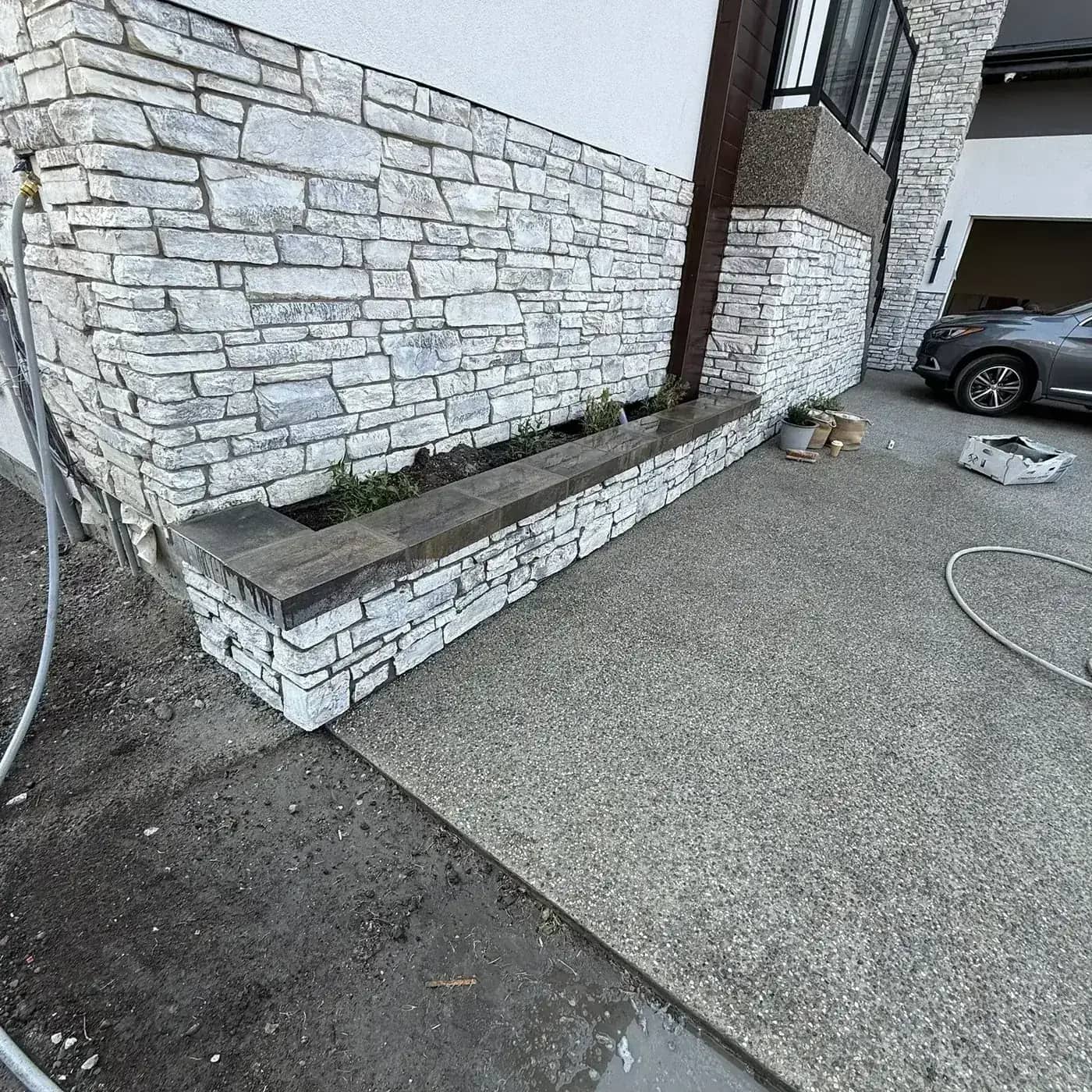 Stone retaining planter wall beside exterior concrete hardscape
