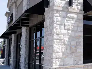 Commercial storefront with light stone masonry columns, black awnings, glass windows, and concrete sidewalk