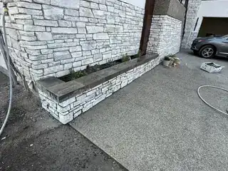 Stone retaining planter wall beside exterior concrete hardscape